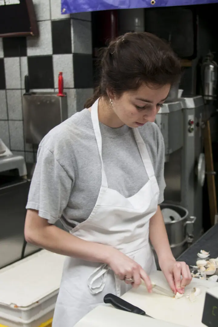 A woman in an apron cutting food on top of a table.